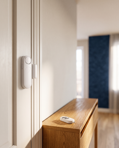 Alarme de porte et fenêtre magnétique blanche TravelShield installée en haut d'une porte, télécommande sur la console