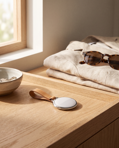 Traceur Bluetooth rond TravelShield sur son anneau en cuir, posé sur une console en chêne