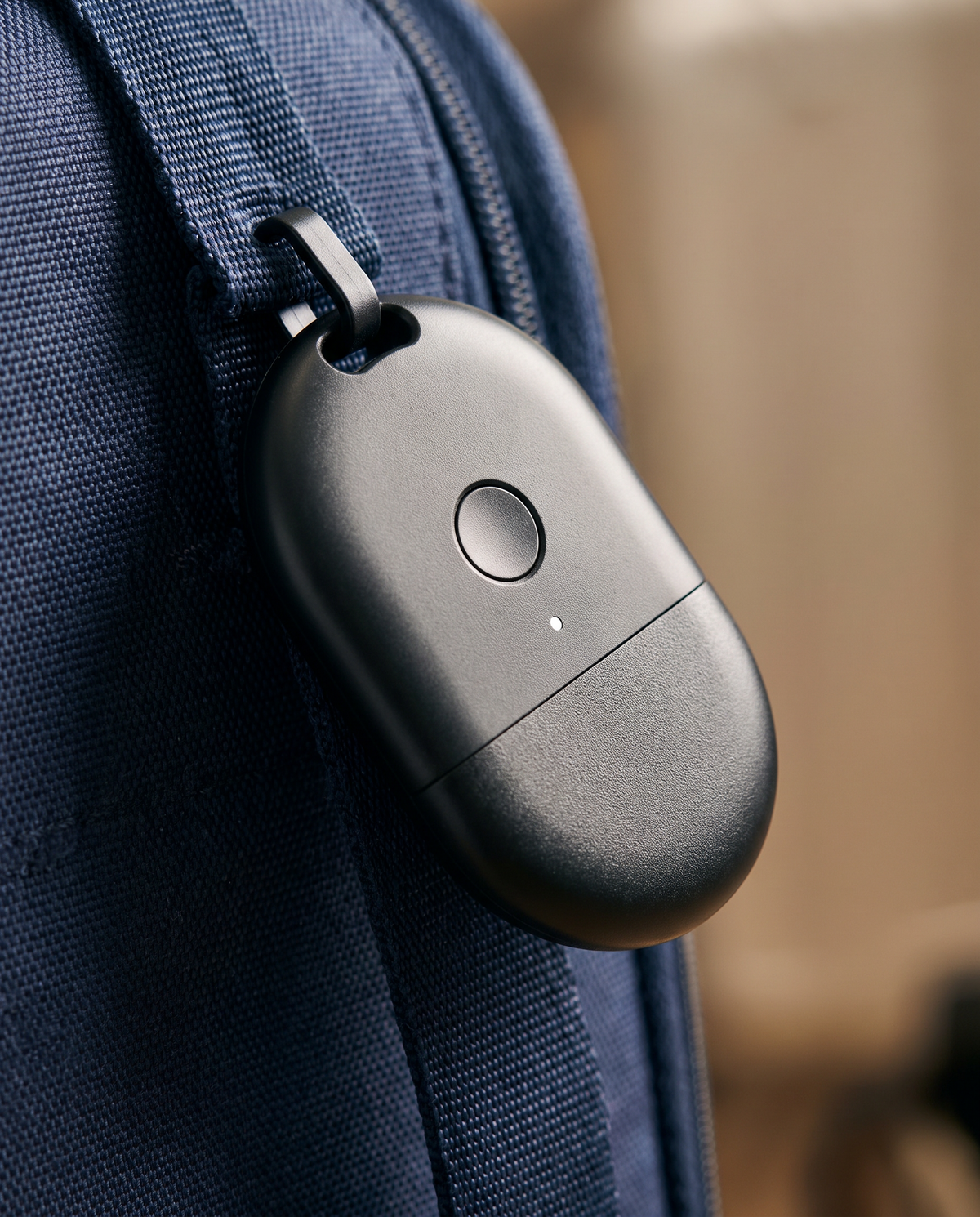 Gros plan sur le traceur Bluetooth clipsé à la sangle d'un sac, boîtier mat et voyant lumineux